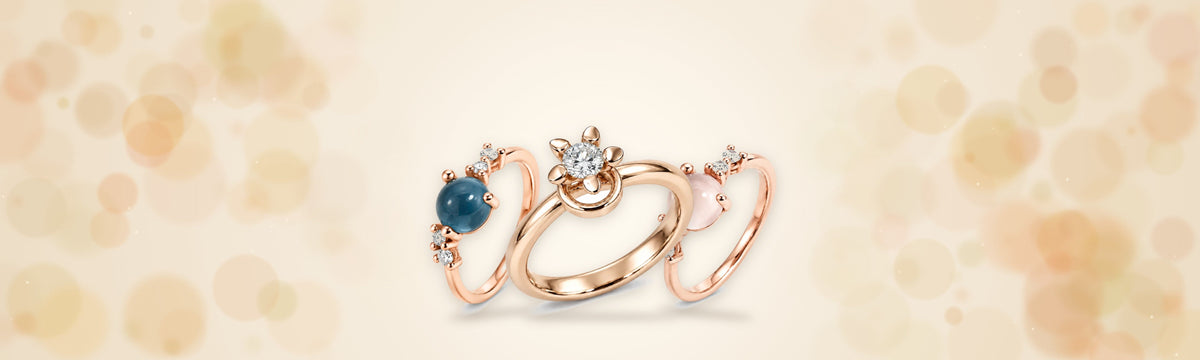 Noën Ringe Love 5 und Stellini aus 18 Karat Fairmined-Roségold vor goldenen Lichtern